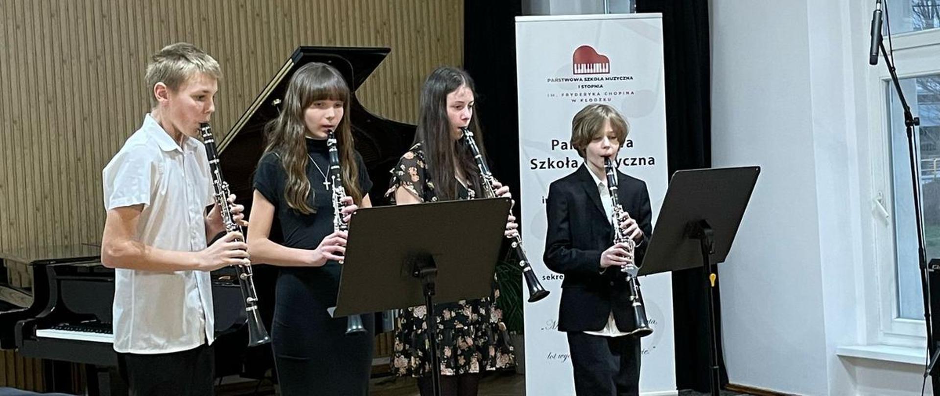 Galeria 21 zdjęć z koncertu szkolne prezentacje młodych kameralistów, który odbył się 26 marca 2025 w auli PSM w Kłodzku. Młodzi wykonawcy grają na instrumentach na scenie sali koncertowej.