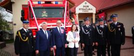 Na zdjęciu widzimy przedstawicieli władz rządowych i samorządowych, zastępcę podkarpackiego komendanta wojewódzkiego PSP oraz komendanta powiatowego PSP stojących przed przekazanym samochodem pożarniczym Mercedes Unimog. W tle widać strażaków OSP oraz remizę OSP Jodłówka.