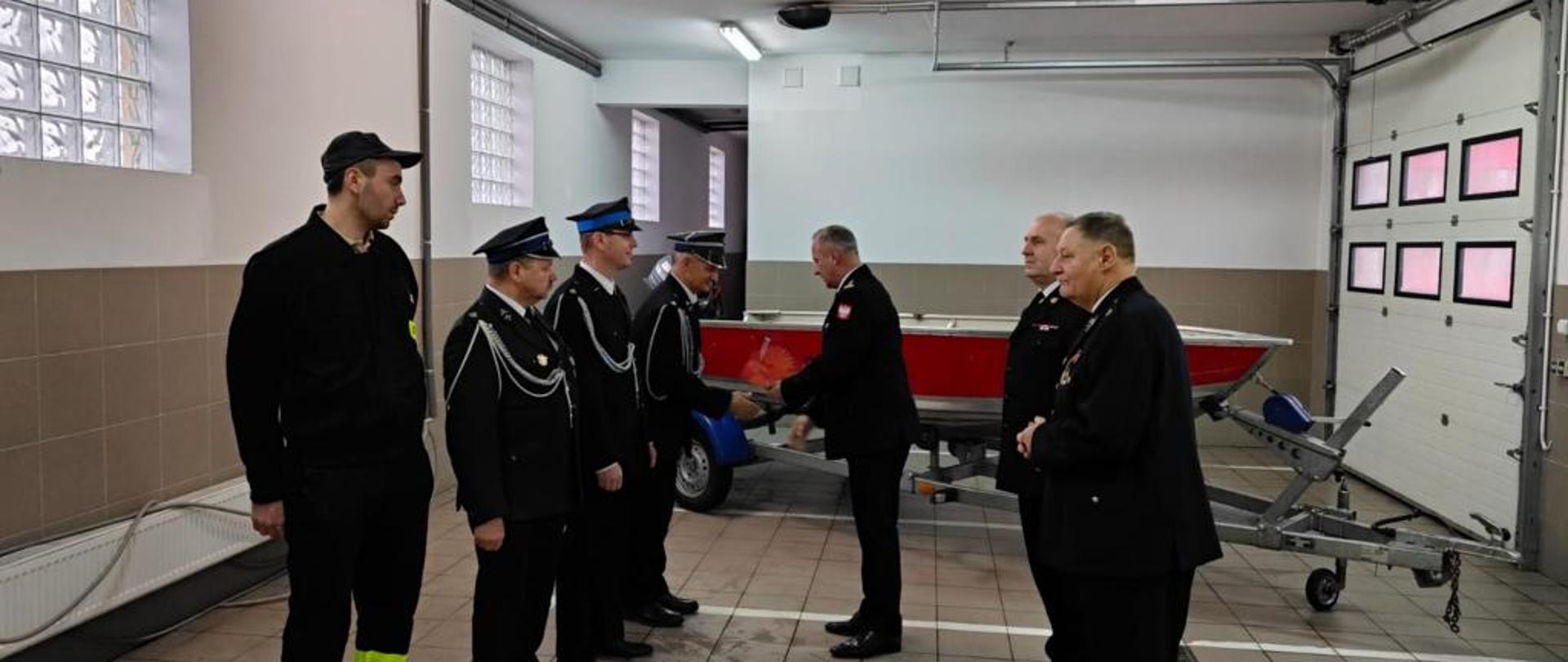 Zastępca Kujawsko-Pomorskiego Komendanta Wojewódzkiego Państwowej Straży Pożarnej starszy brygadier Robert Wiśniewski na jednym z garaży Komendy Powiatowej Państwowej Straży Pożarnej w Rypinie gratuluje i przekazuje łódź przedstawicielom Ochotniczej Straży Pożarnej w Starym Kobrzyńcu.