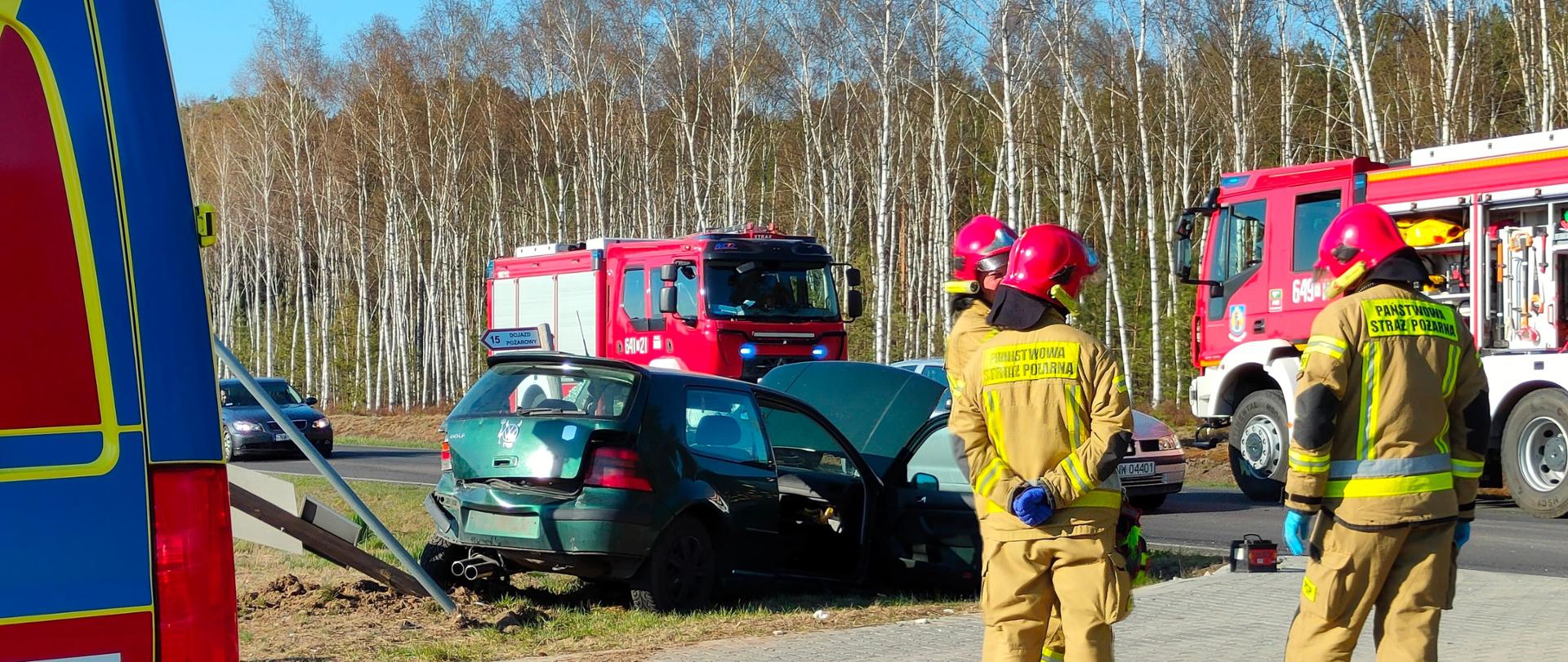 Na zdjęciu widać stojących strażaków. Na drugim planie rozbite samochody.