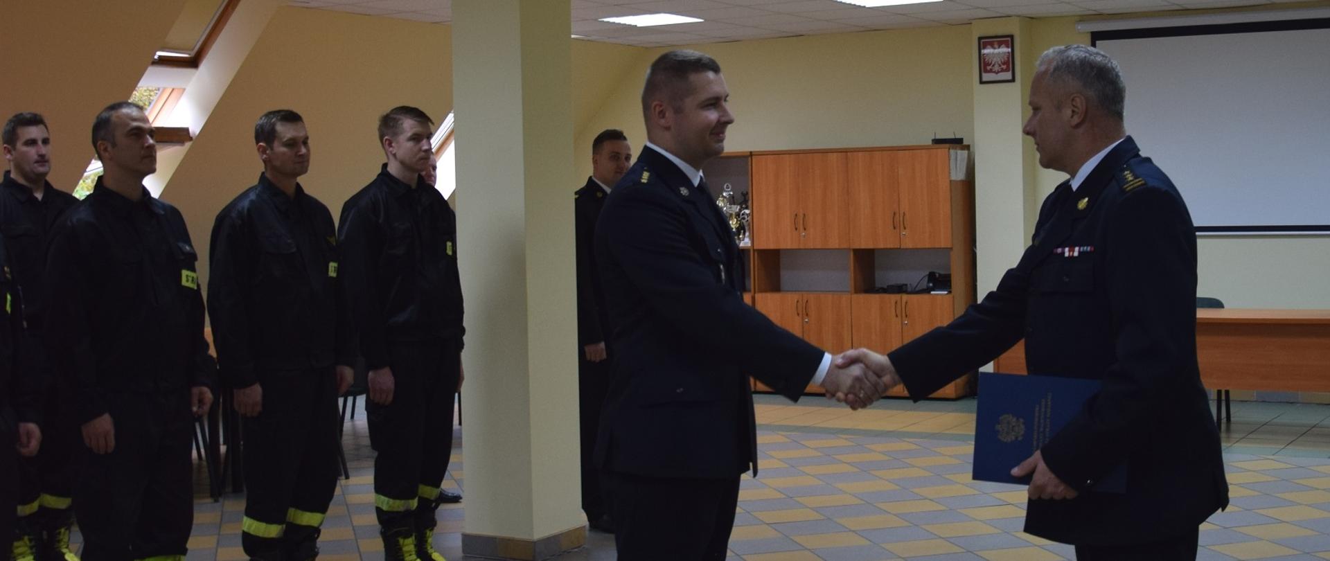 Na zdjęciu widać zastępcę kujawsko-pomorskiego komendanta wojewódzkiego PSP, wręczającego wyróżnienie strażakowi. W tle w dwuszeregu stoją strażacy.