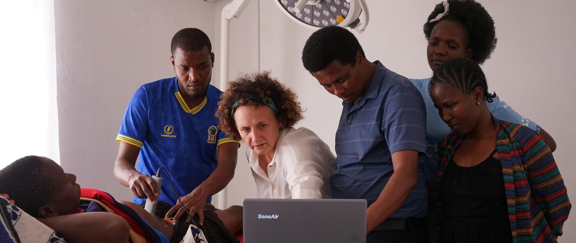 Lekarka pokazuje jak wykonać badanie na leżącym pacjencie, wykonywane jest usg, 4 osoby obserwują jej pracę