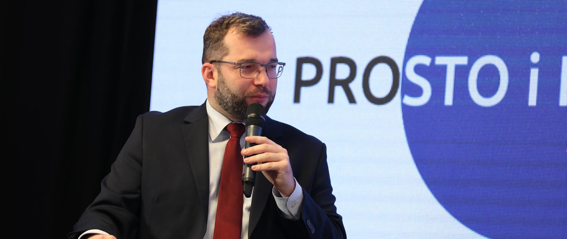 minister Grzegorz Puda mówi do mikrofonu, za nim napis Prosto i kropka