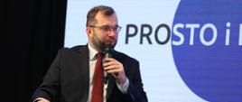minister Grzegorz Puda mówi do mikrofonu, za nim napis Prosto i kropka
