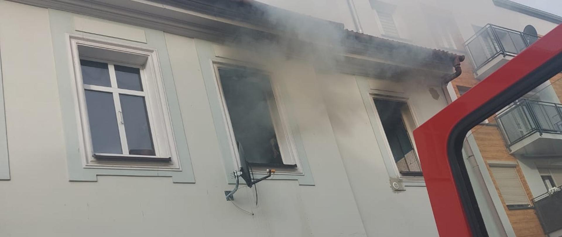 Zdjęcie przedstawia wydobywający się dym z okien mieszkania.