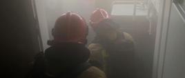 Wnętrze biurowca, strażacy prowadzący działania gaśnicze w zadymieniu.