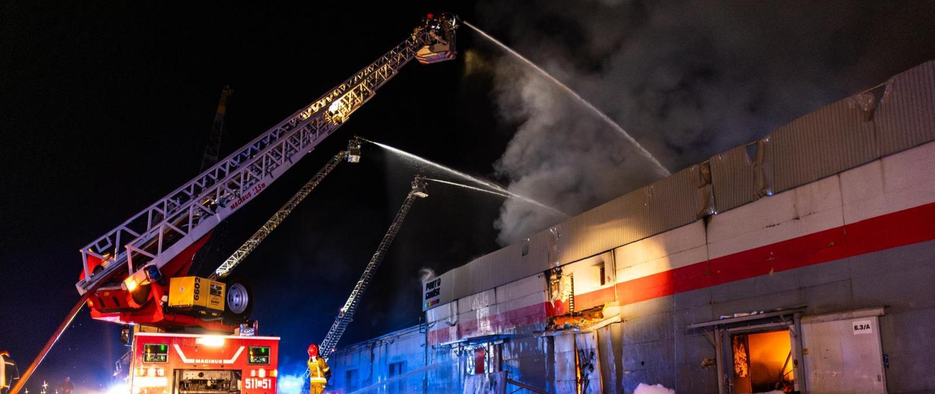 Widok na palącą się halę i 3 drabiny mechaniczne podające wodę z działek na halę.