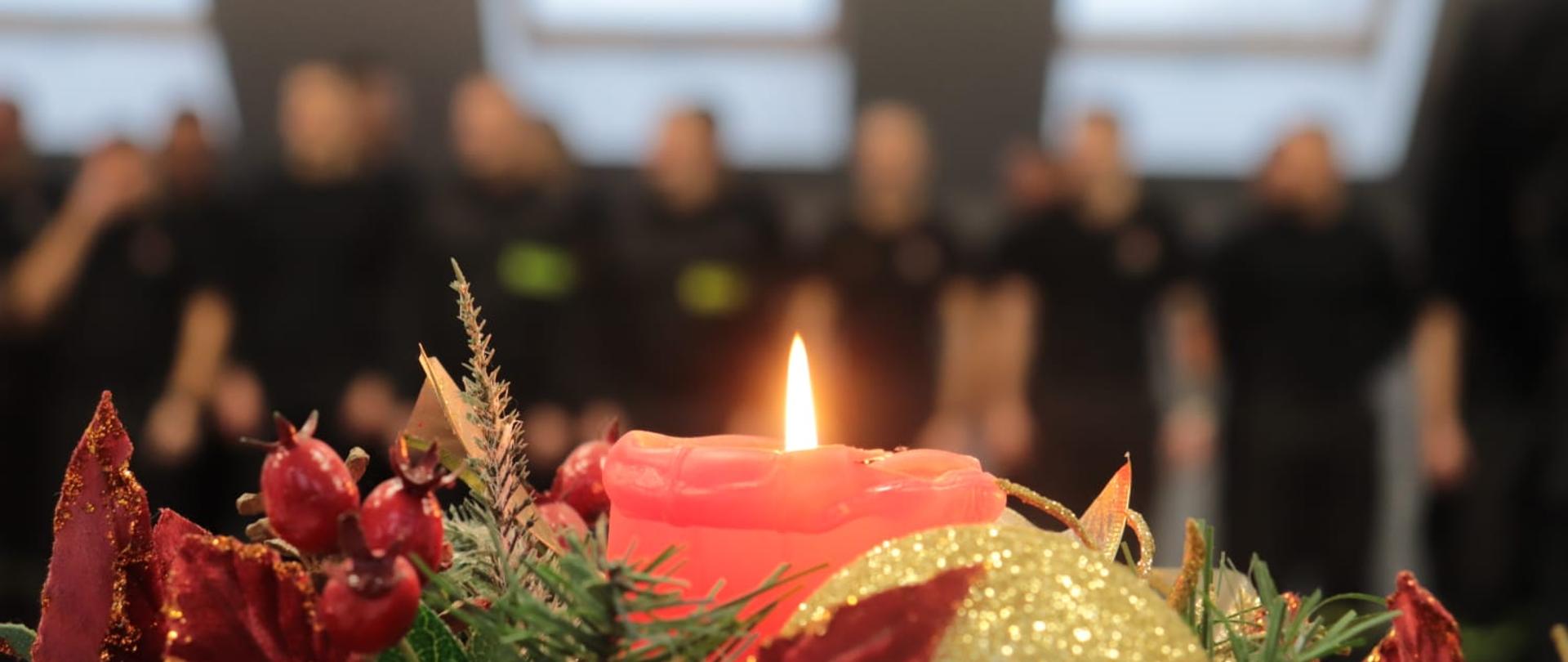 Na pierwszym planie płonąca świeca wigilijna, w tle strażacy w pododdziale 