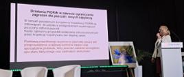 Inspektor na scenie omawia działania inspekcji w zakresie ograniczania zagrożeń dla pszczół i innych zapylaczy. W tle znajduje się prezentacja i zdjęcie pszczoły.