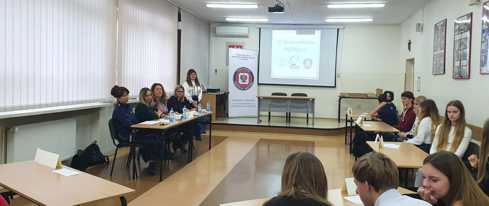 Pomieszczenie, uczestnicy zastanawiają się nad udzieleniem odpowiedzi na zadane pytanie.