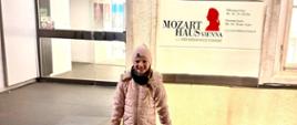 Zdjęcie przedstawia Marię Kaczmarek stojącą przed wejściem do Domu Mozarta w Wiedniu.