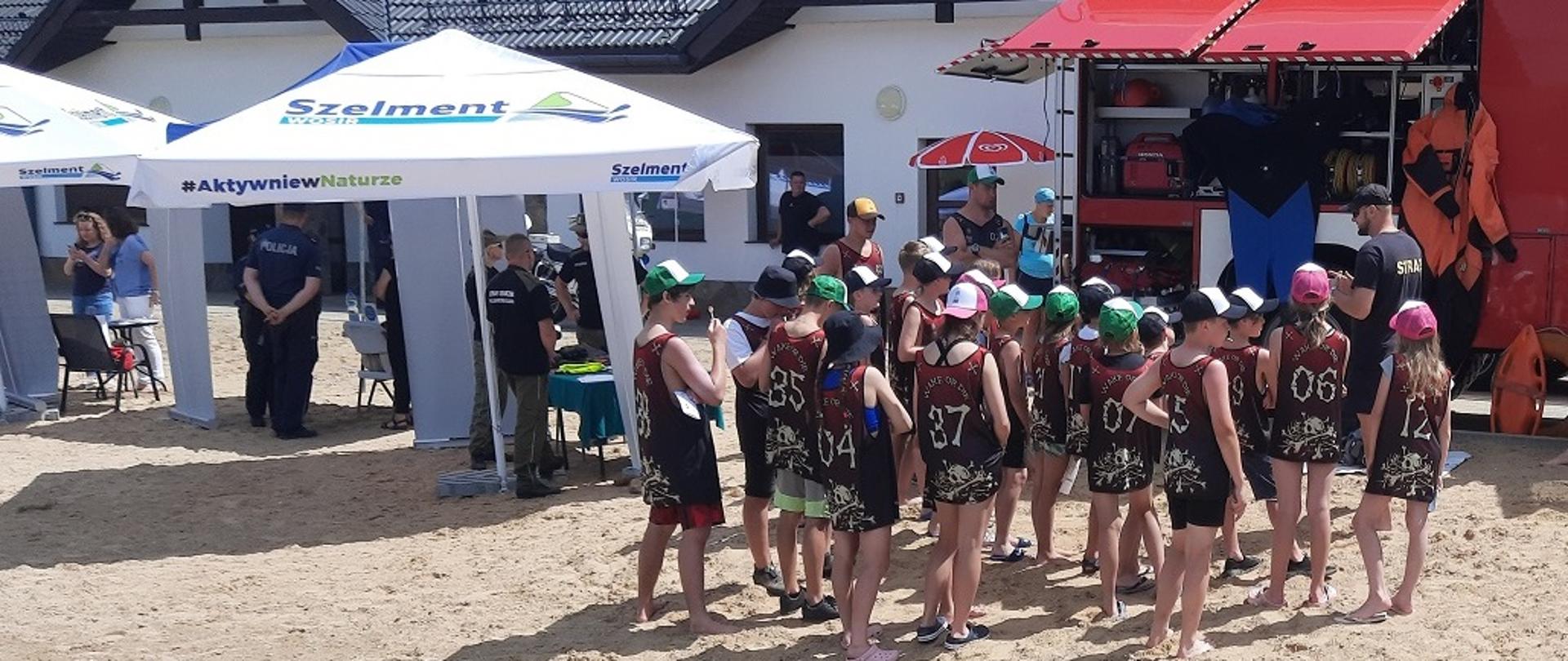 Na zdjęciu widać samochód strażacki namioty dzieci i funkcjonariuszy w tle budynek