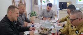 Przedstawiciele Państwowej Straży Pożarnej i partnerów instytucjonalnych podpisują dokumenty podczas spotkania roboczego w gabinecie.