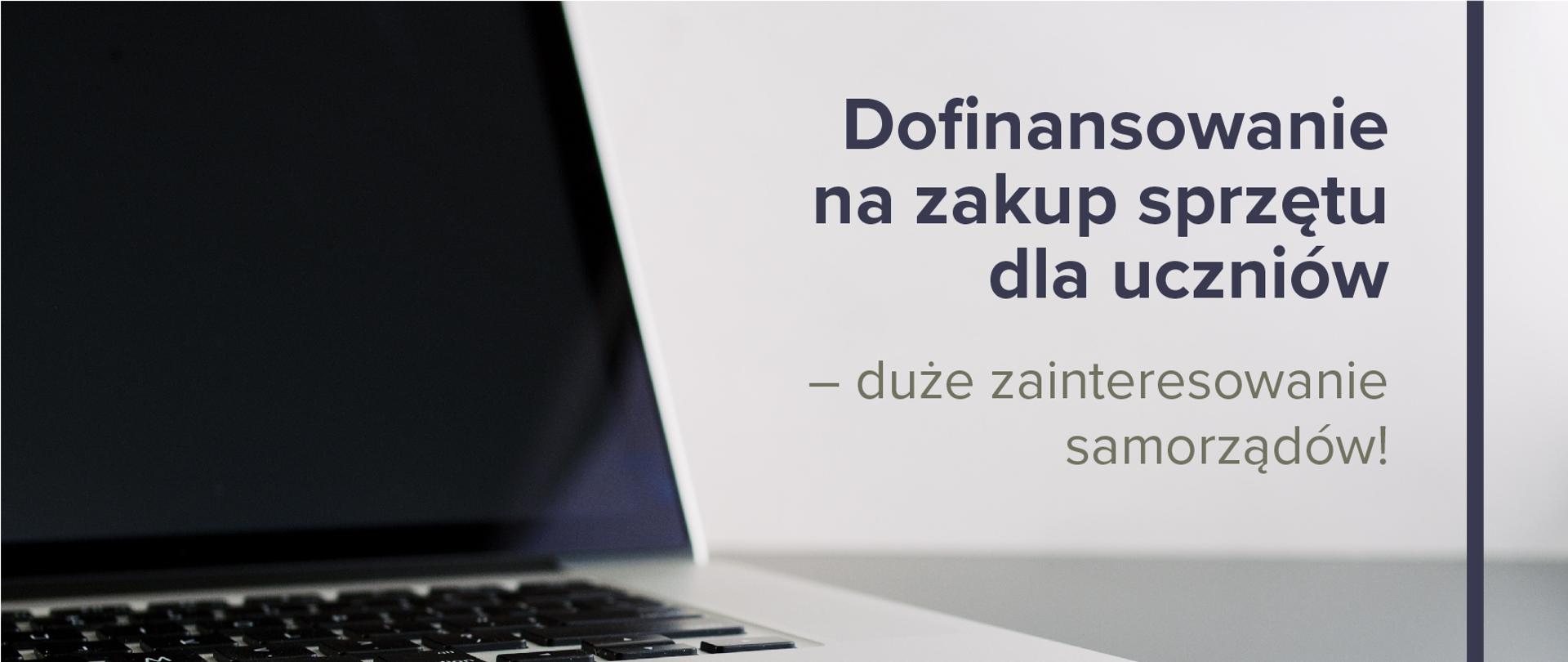 Otwarty laptop z czarnym ekranem po lewej stronie. Po prawo napis na białej ścianie:
Dofinansowanie na zakup sprzętu dla uczniów – duże zainteresowanie samorządów!
