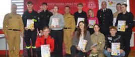 Świetlica komendy. Na tle ścianki promocyjnej wraz z organizatorami do pamiątkowego zdjęcia pozują uczestnicy eliminacji z najstarszej grupy wiekowej. Trzymają w rękach dyplomy i upominki. 