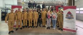 Strażacy i rodzina odchodzącego na emeryturę aspiranta Adama Sarbiewskiego stoją w garażu JRG - pamiątkowe zdjęcie grupowe.