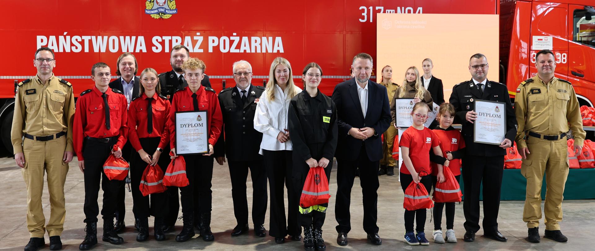 Pamiątkowe zdjęcie młodzieży z Młodzieżowych Drużyn Pożarniczych w mundurach z Ministrem SWiA i pozostałymi wręczającymi.