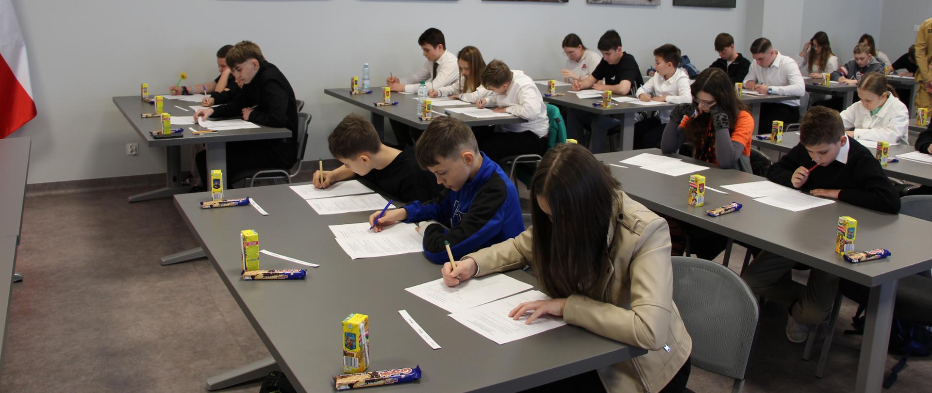 Zdjęcie przedstawia dzieci i młodzież szkolna podczas pisania testu