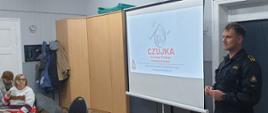 Strażak przeprowadza pogadankę z seniorami na temat bezpieczeństwa zakresie ochrony przeciwpożarowej, czujek i pożarów.