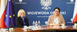 Na zdjęciu widać Dyrektor Wydziału Zdrowia Mirosława Kwatek-Hoffmann oraz Wojewoda Opolski Monika Jurek. Siedzą przy stole. W tle widać granatowy baner z napisem Wojewoda Opolski. Po lewej stronie widać również flagę Polski oraz Unii Europejskiej. 