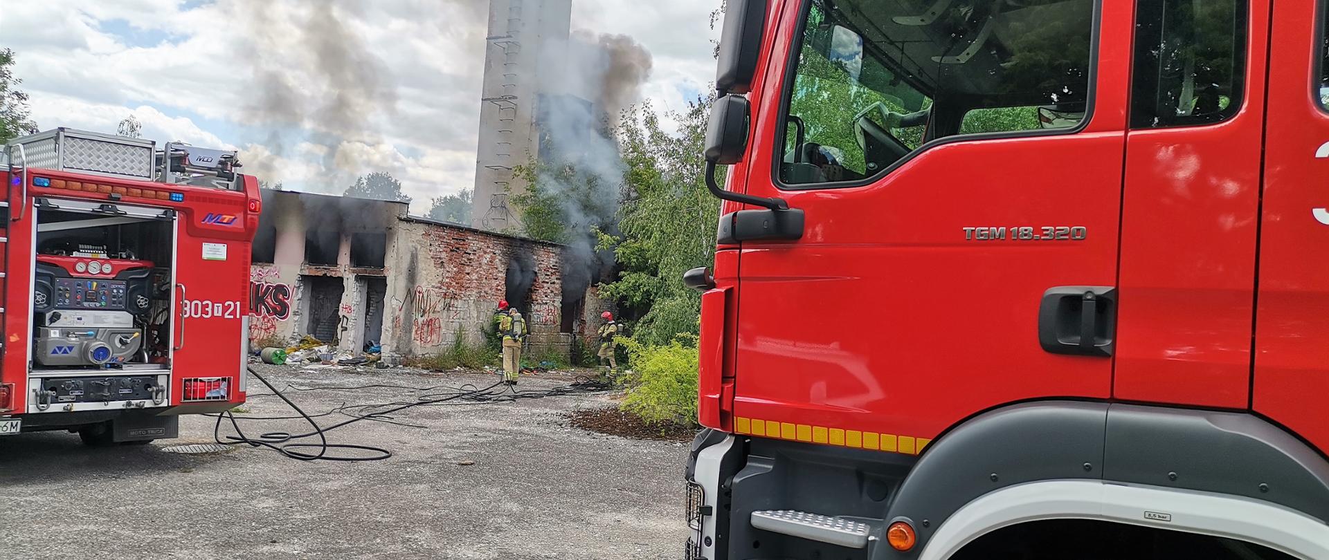 Zdjęcie prezentuje stojące z dwóch stron samochody gaśnicze, a w centralnym punkcie znajduje się zdewastowany budynek kotłowni. Przez otwory okienne wydostają się kłęby czarnego dymu. Przy budynku grupa 3 strażaków. 