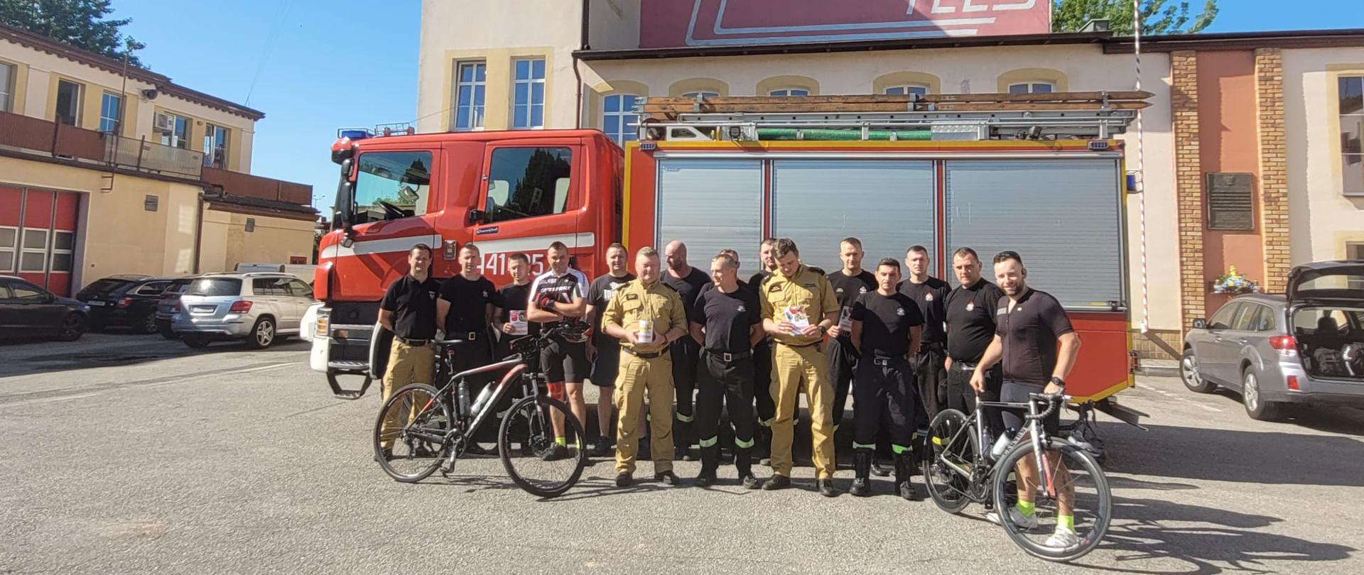 Zdjęcie przedstawia strażaków i osoby uczestniczące w zbiórce, w tle samochód pożarniczy 