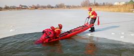 Na zdjęciu widać trzech funkcjonariuszy Państwowej Straży Pożarnej podczas wydobywania osoby pod którą zarwał się lód przy wykorzystaniu sań lodowych. 