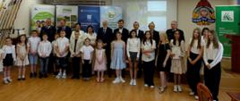 Grupa kilkunastu laureatów konkursów pozuje do zdjęcia w sali konferencyjnej wraz z przedstawicielami współorganizatorów stojącymi w drugim rzędzie. Za nimi rollupy z logo KRUS.