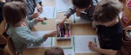 dzieci siedzą przy stoliku i kolorują obrazki
