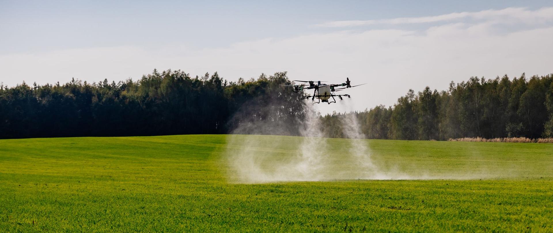 Dron rolniczy rozpylający substancję nad zielonym polem, wykorzystujący nowoczesne technologie w rolnictwie precyzyjnym. Zdjęcie: ZSCKR, A. Kawalec.