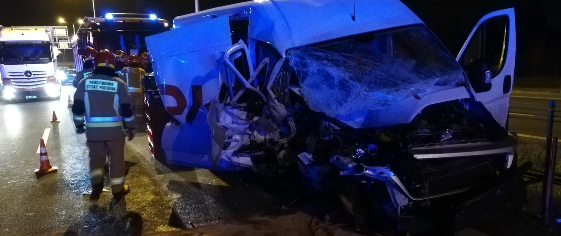 Na zdjęciu widoczny jest uszkodzony samochód dostawczy służy dogowej, radiowóz policji pracujący strażacy w tle samochód straży pożarnej 