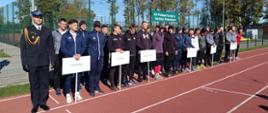 Za nami XVI Podlaski Turniej w Dwuboju Pożarniczym - sportowcy stojący w szeregu, ubrani w dresy - stoją na bieżni i trzymają tabliczki z nazwami województw