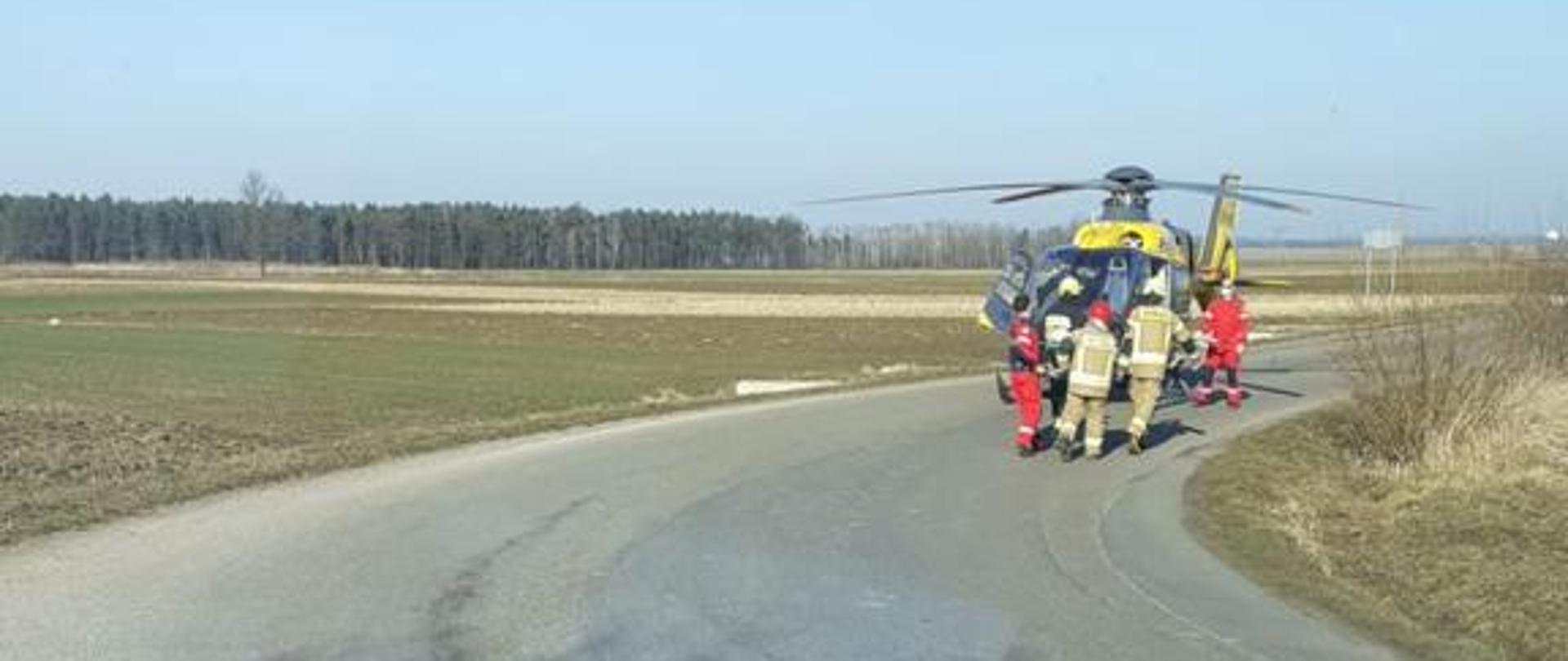 Śmigłowiec LPR na drodze, przed śmigłowcem strażacy i obsługa śmigłowca.