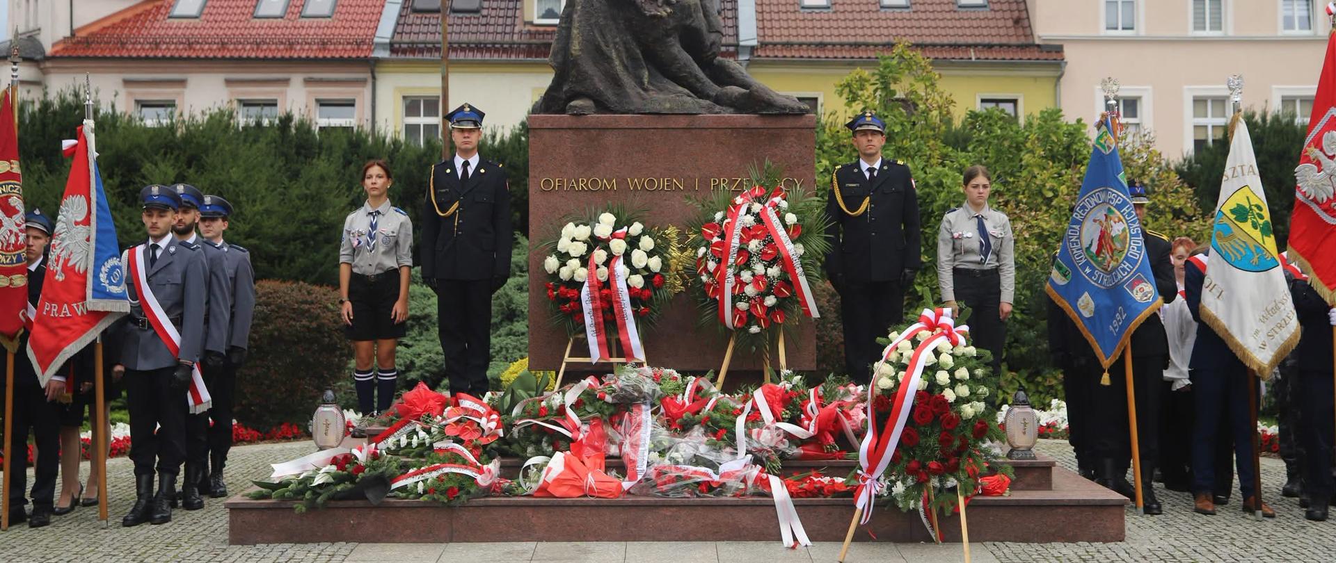 Na zdjęciu znajdują się funkcjonariusz służb w umundurowaniu, poczty sztandarowe, warta honorowa przy pomniku