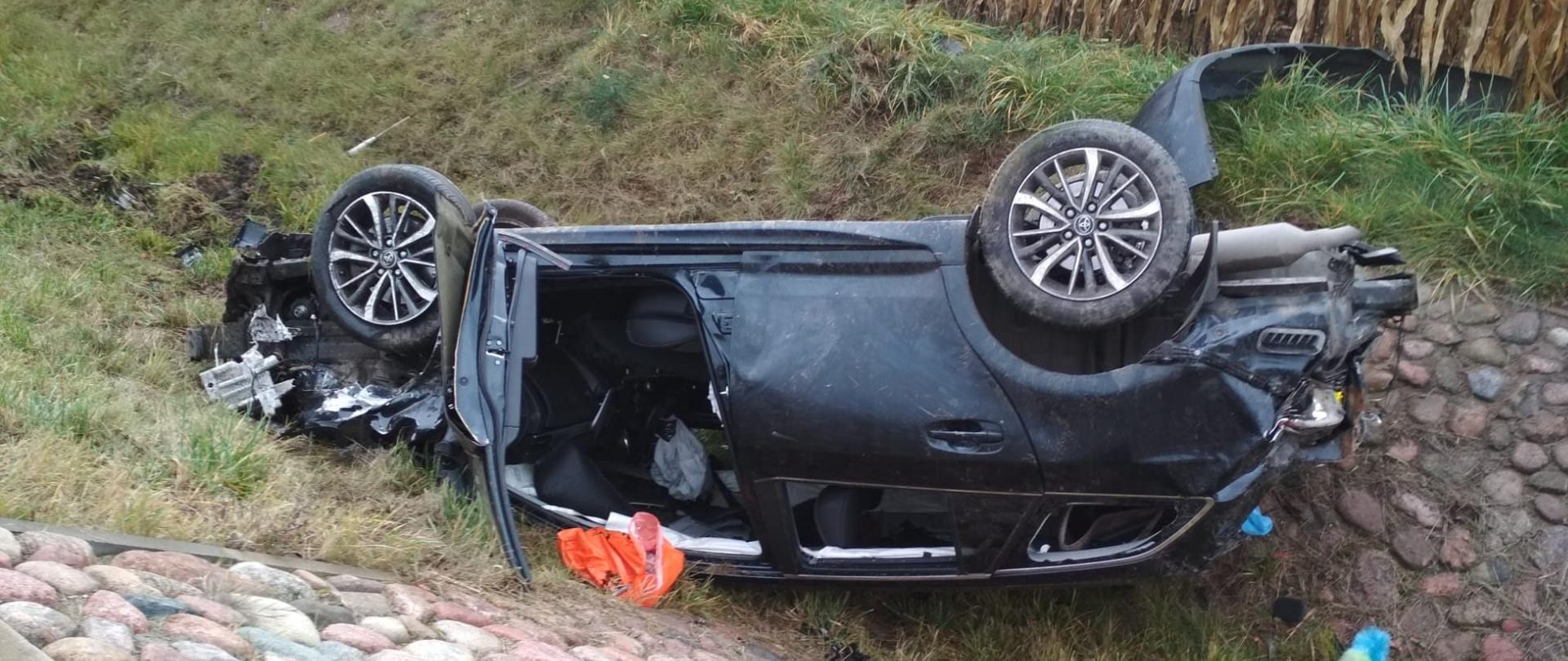 Zdjęcie przedstawia samochód osobowy na dachu w rowie