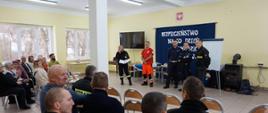 Strażacy Policjant i pracownik PCK przemawiający do zgromadzonych mieszkańców