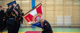 Nowo powołany komendant szkoły aspirantów klęczy na jedno kolano i oddaje honor sztandarowi szkoły całując płat sztandaru