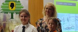 Zdjęcie przedstawia dwie uczennice wraz z nauczyciel Panią Karoliną Skrzypczyńską stojących na scenie podczas warsztatów skrzypcowych.