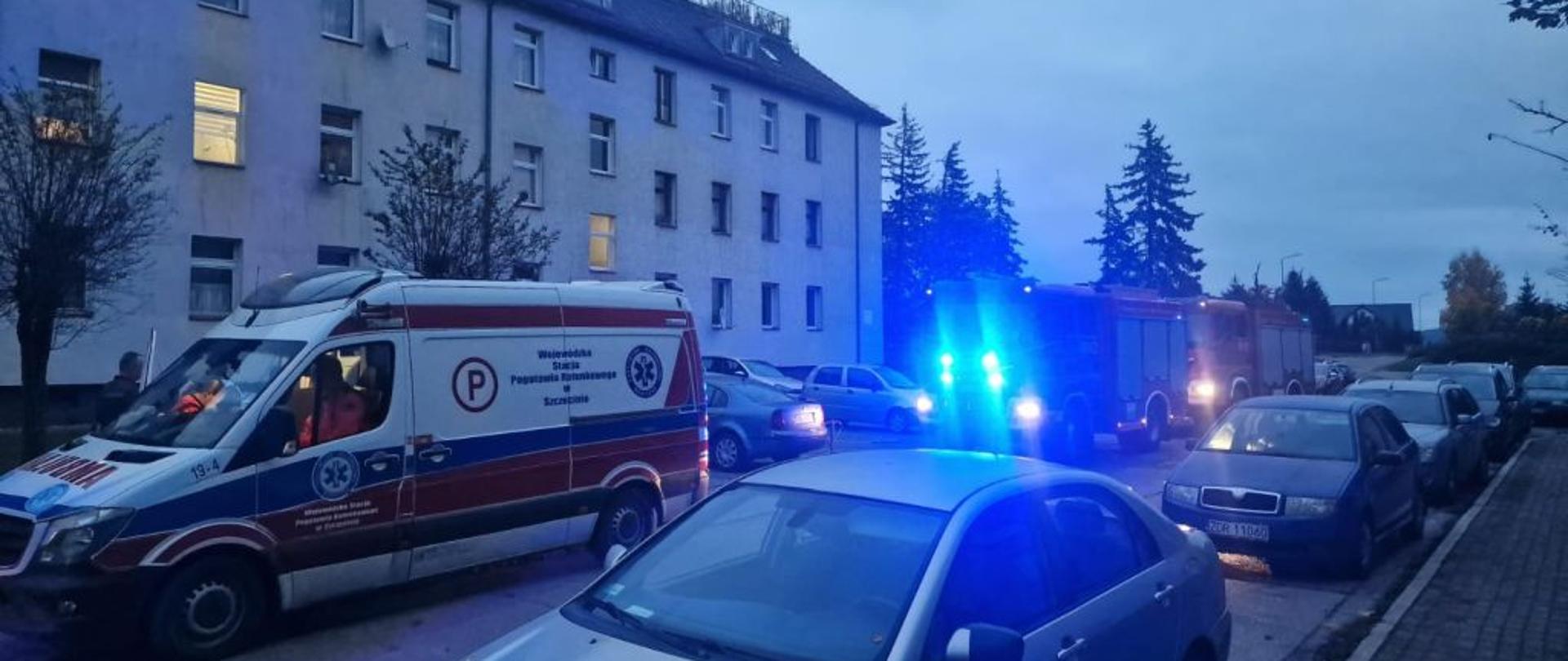 Widok na zaparkowane przed budynkiem auta uczestniczące w zdarzeniu. W tle budynek w którym doszło do zdarzenia. Budynek wysoki, biały.