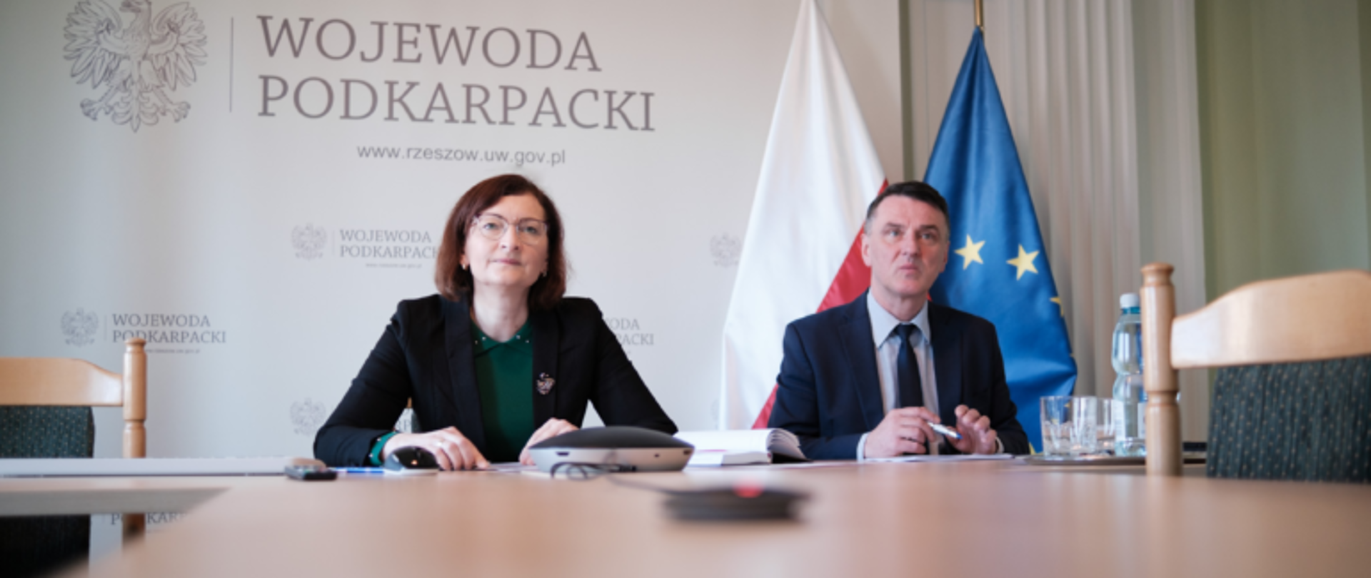 Wojewoda podkarpacki Ewa Leniart i dyrektor generalny Podkarpackiego Urzędu Wojewódzkiego w Rzeszowie Marcin Zaborniak przy stole prezydialnym podczas narady z parlamentarzystami. W tle baner z napisem Podkarpacki Urząd Wojewódzki w Rzeszowie.