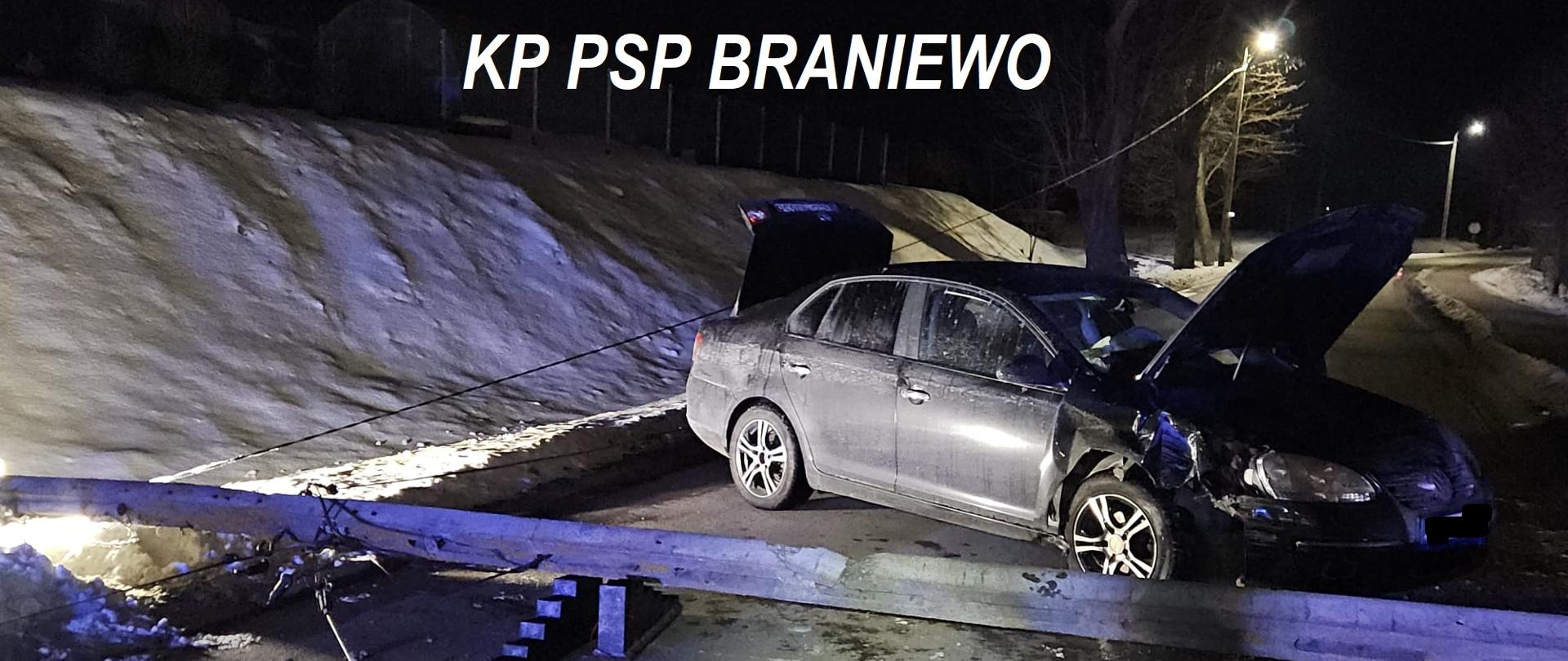 Zdjęcie zrobione nocą. W poprzek drogi stoi ciemne auto osobowe. Dodatkowo w poprzek drogi leży betonowy słup.