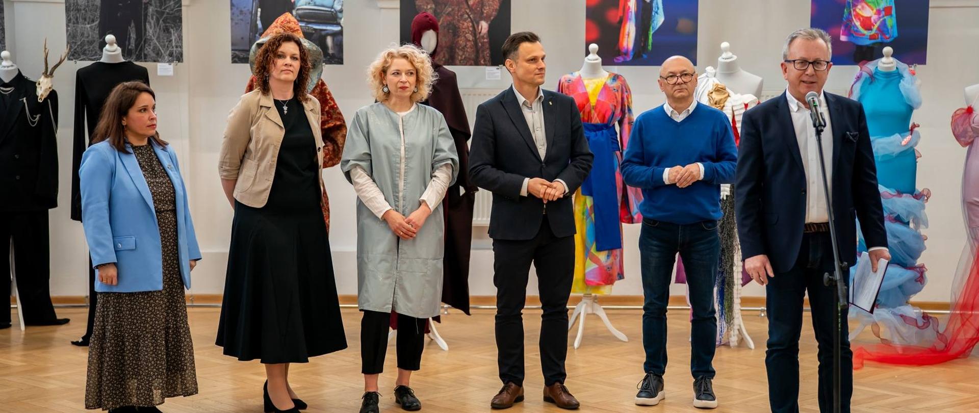 Na zdjęciu stoi sześć osób a w tle widać prace plastyczne