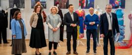 Na zdjęciu stoi sześć osób a w tle widać prace plastyczne