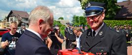 Wojewoda pomorski wręcza pamiątkowy upominek strażakowi ochotniczej straży pożarnej.