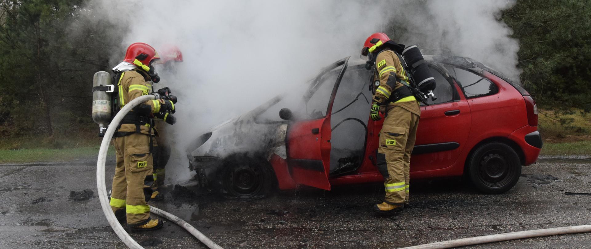 strażacy gaszą samochód osobowy koloru czerwonego
