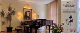 Scena auli PSM I st. w Kłodzku z widocznym fortepianem, kwiatami oraz banerem XXVI Kłodzkiego Konkursu Pianistycznego 17-18 maja 2024