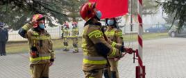 Na zdjęciu widoczni są 3 strażacy w ubraniu bojowym , strażacy podnoszą flagę RP na maszcie. 