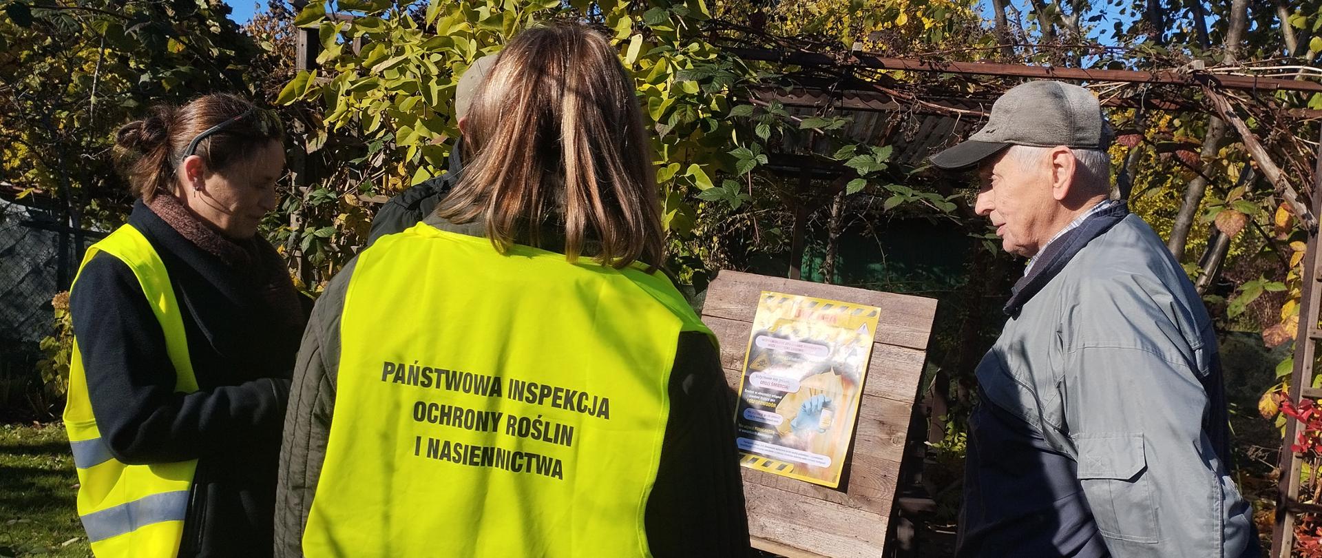 trzy osoby stoją przy tablicy ogłoszeniowej pośród roślin