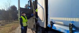 Inspektor wielkopolskiej ITD stoi obok drzwi kabiny zatrzymanej do kontroli ciężarówki i pobiera dokumenty od kierowcy.
