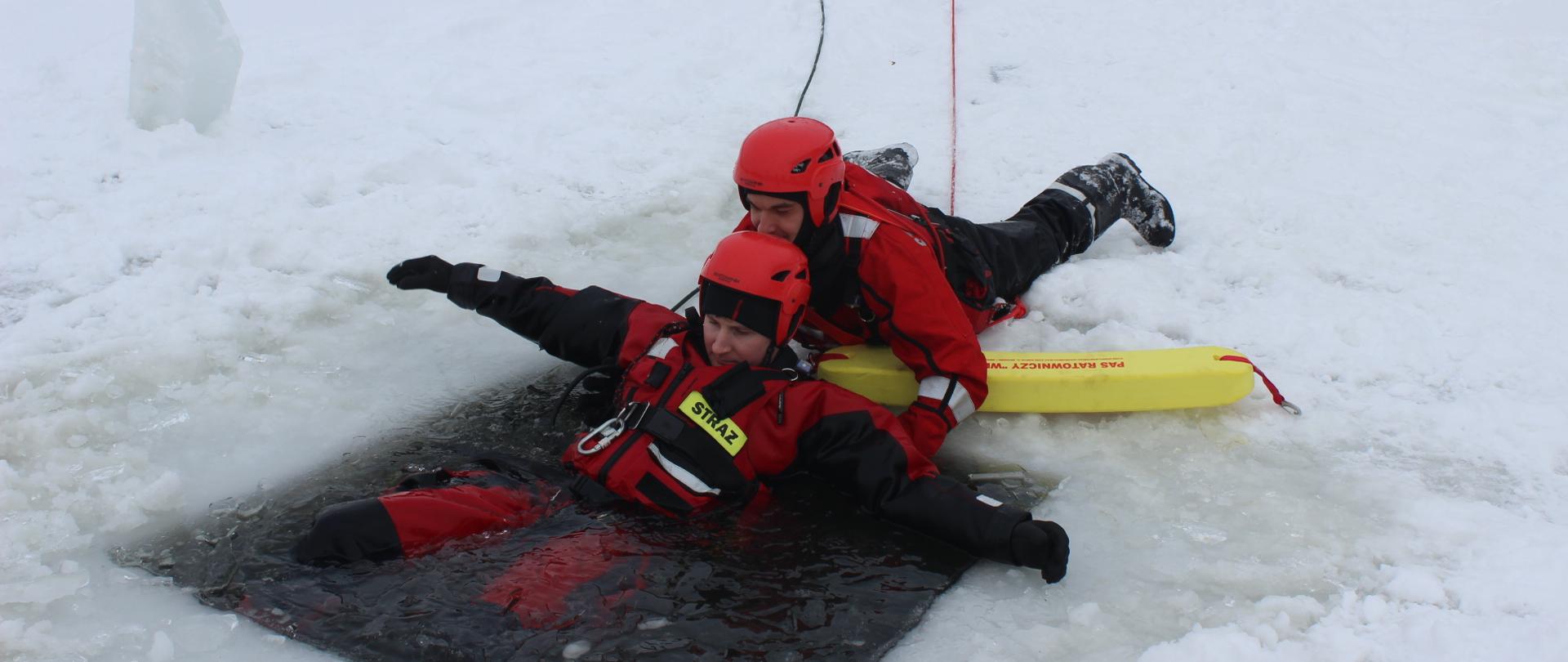 strażak wyciąga z przerębli pozoranta przy użyciu pasa ratowniczego. Strażak leży zabezpieczony linką ratowniczą